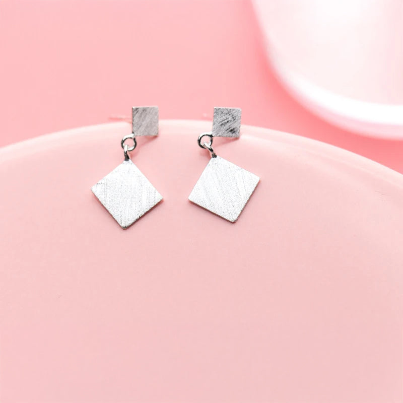 Close up of geometric dangle earrings with frosted texture and hook earrings detail