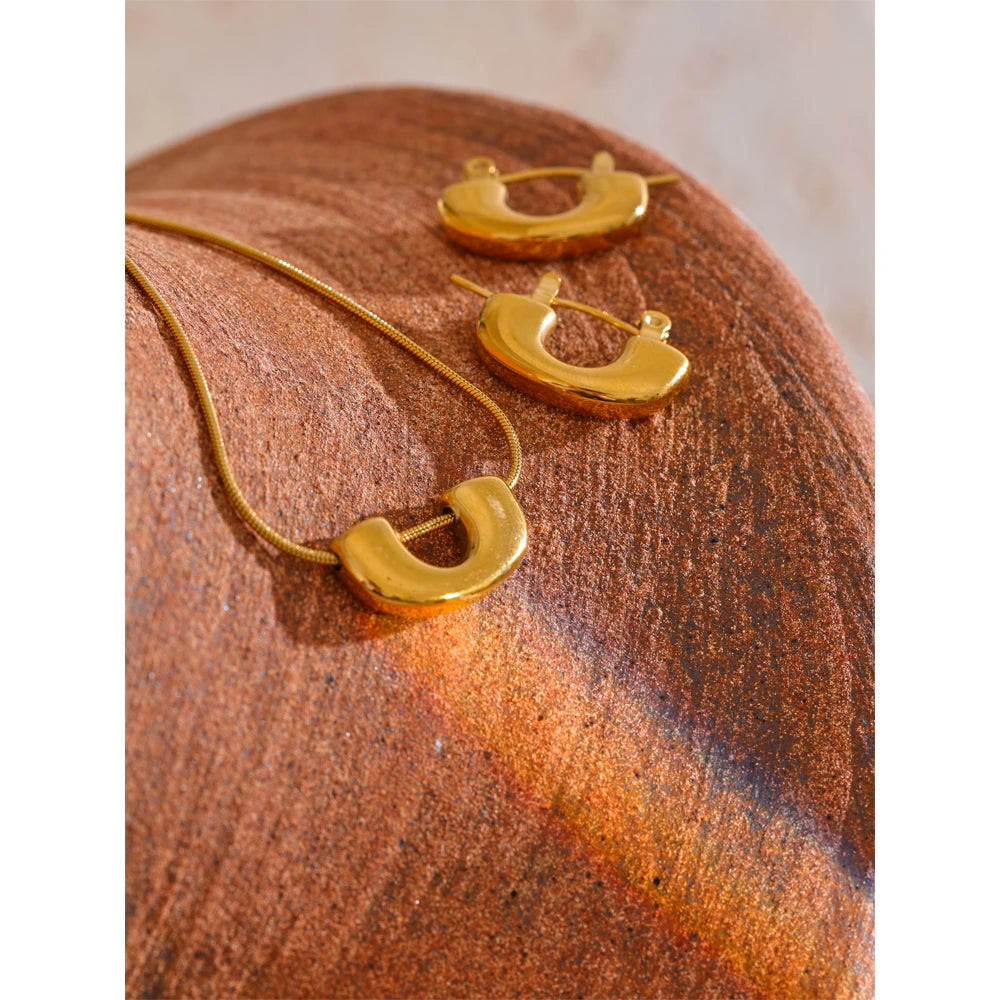 Model wearing gold i necklace pendant from a necklace and earrings set