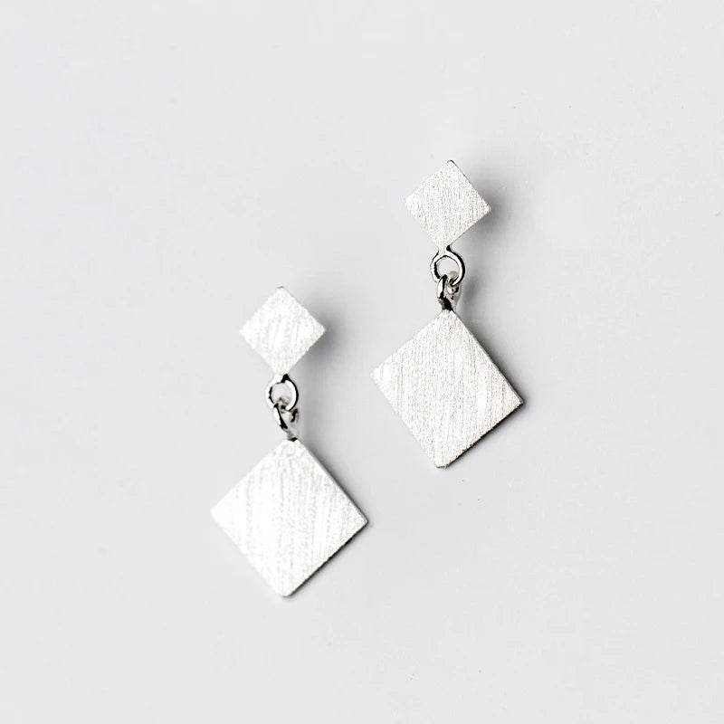 Frosted geometric long dangle earrings photographed against white showing silver color finish