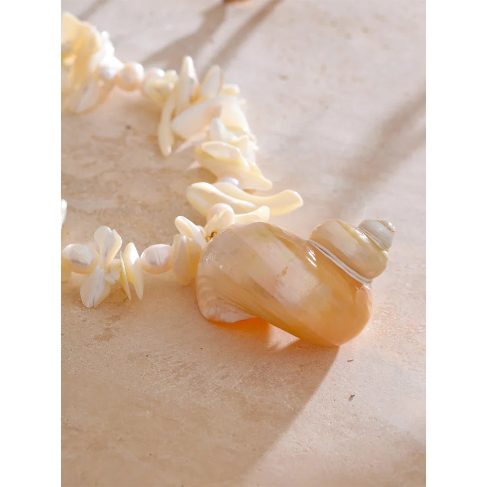 Close-up of pendant necklace showing conch shell detail and pearl charm in gold tone
