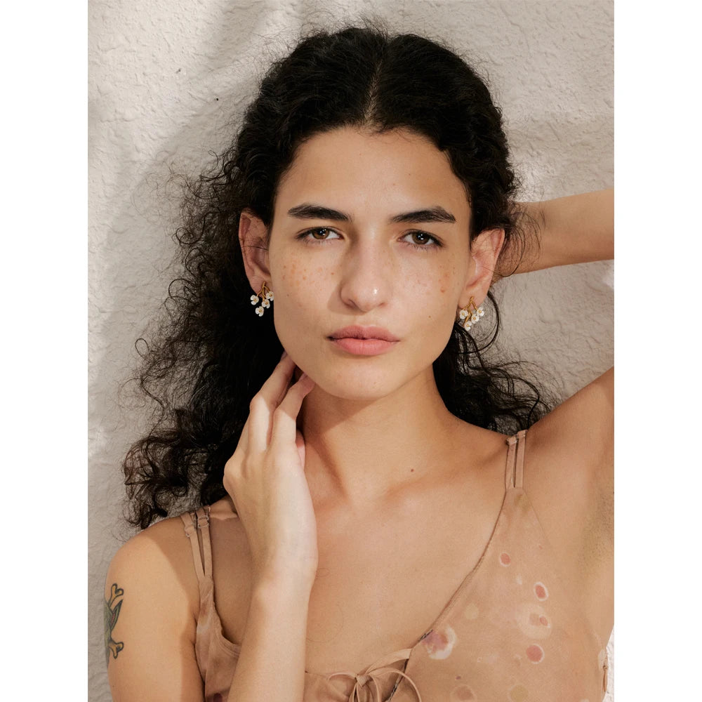 Close up of stud earrings with flower in gold detail and polished gold plated finish