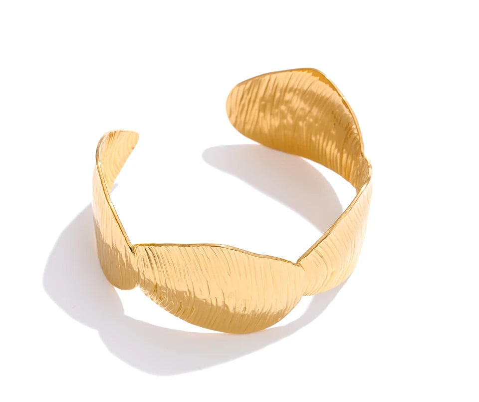 Fashion image of gold cuff stacked with a bracelet charm accent