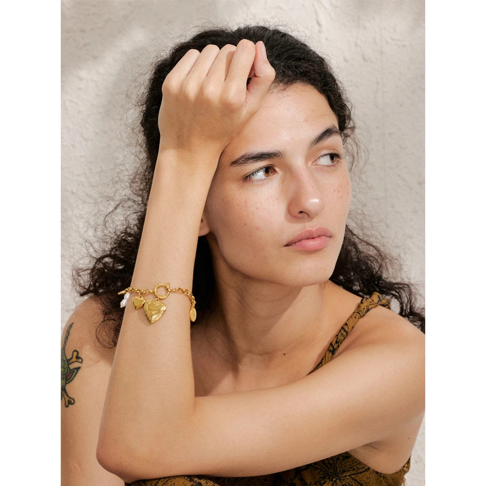 Gold plated chain bracelet layered with charms and bracelets on the wrist